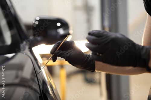 confident auto mechanic man using brush for painting a car, applying paint of black representative automobile after scratching