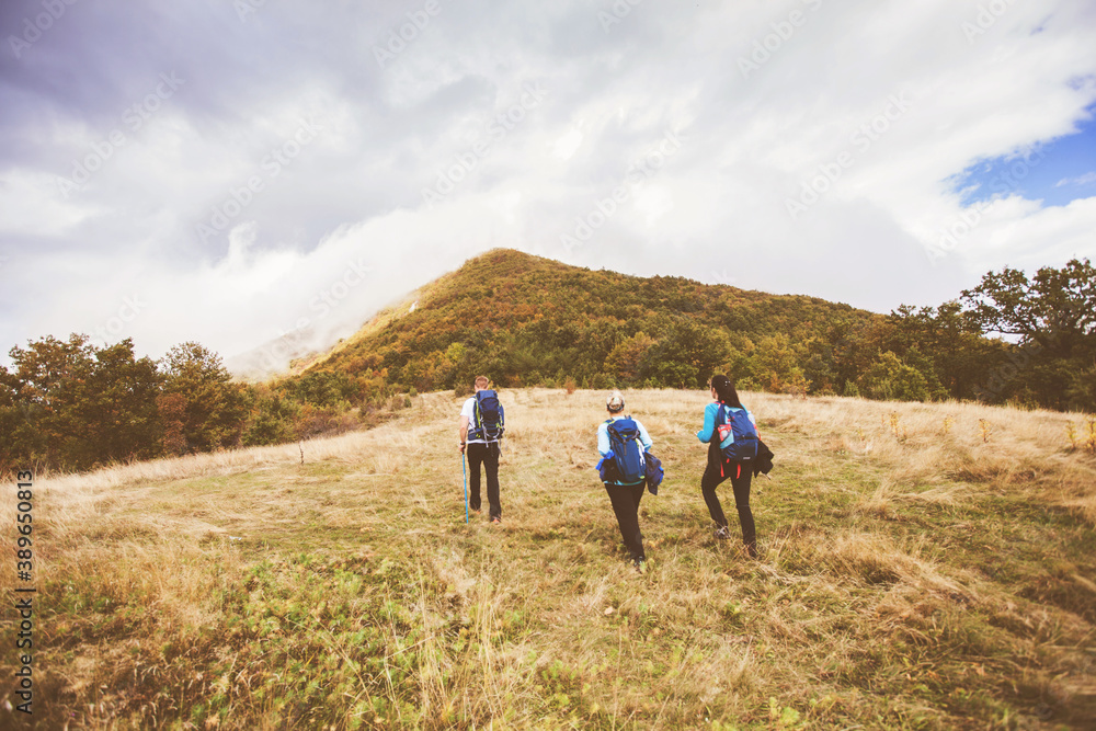 Group of active people hiking on autumn day through beautiful nature landscape. Misty Mountain Peak. Rear View. Cloudy sky in the background.