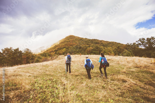 Group of active people hiking on autumn day through beautiful nature landscape. Misty Mountain Peak. Rear View. Cloudy sky in the background.