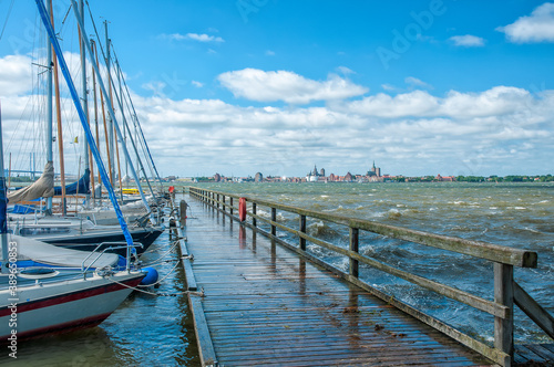 Festgemachte Segelboote mit Steg im Hafen von Altefähr auf Rügen mit der Stadt Stralsund am Horizont.