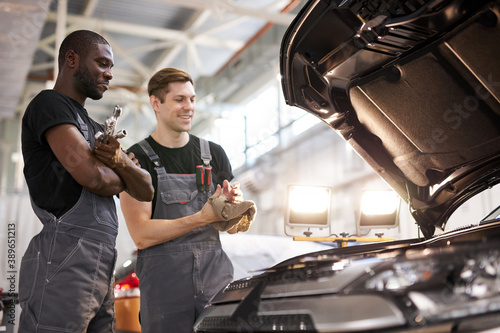 two friendly professional auto mechanic during work, they are successfully repairing car, solve problems together