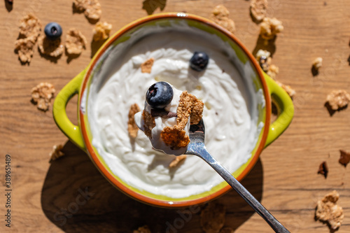 Spoon filled with Greek yogurt, blueberries, muesli with green bowl underneath. Some scattered muesli on counter top. 