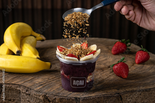 Delicious Brazilian Açaí Cream, in a plastic Cup With Strawberry, banana and granola Topping, in a rustic wooden background. Summer acai smoothie