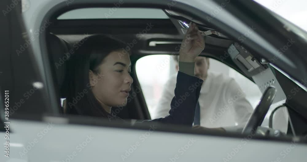 Female in car showroom talking to sales person and looking at automotive vehicle in dealership Female in car showroom talking to sales person and looking at automotive vehicle in dealership