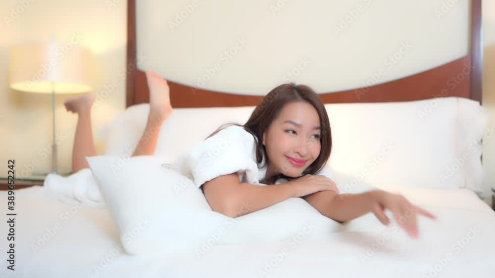 An attractive young beautiful woman flirts with the camera while lying on a hotel suite bed in a terrycloth resort robe. An attractive young beautiful woman flirts with the camera while lying on a hotel suite bed in a terrycloth resort robe.
