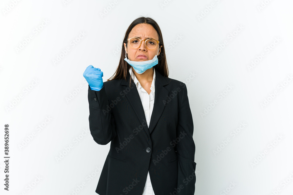 Young business latin woman wearing a mask to protect from covid isolated on white background showing fist to camera, aggressive facial expression. Young business latin woman wearing a mask to protect from covid isolated on white background showing fist to camera, aggressive facial expression.