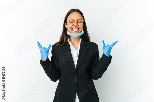 Young business latin woman wearing a mask to protect from covid isolated on white background showing rock gesture with fingers