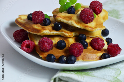 Homemade Belgium Waffles with fresh blueberries for breakfast. White plate, Viennese waffles with raspberries and mint. quick delicious breakfast on white background