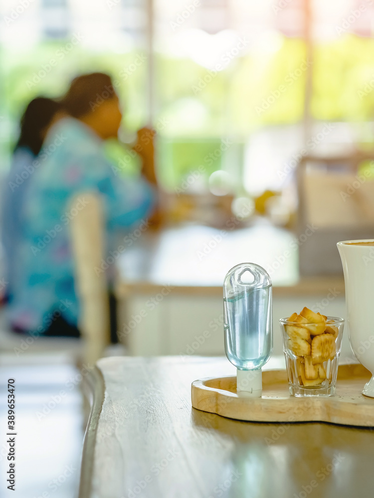 Mini portable alcohol gel bottle to kill Corona Virus(Covid-19) and biscuits and coffee cup on table with blurred image of a family eating at restaurant in background. Health care concept. Mini portable alcohol gel bottle to kill Corona Virus(Covid-19) and biscuits and coffee cup on table with blurred image of a family eating at restaurant in background. Health care concept.