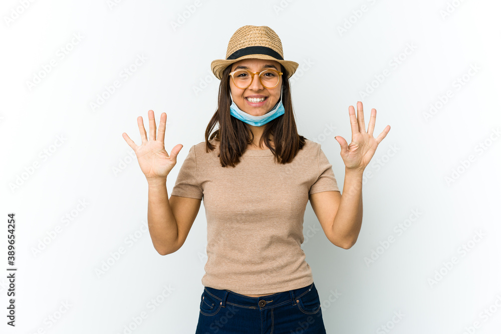 Young latin woman wearing hat and mask to protect from covid isolated on white background showing number ten with hands. Young latin woman wearing hat and mask to protect from covid isolated on white background showing number ten with hands.