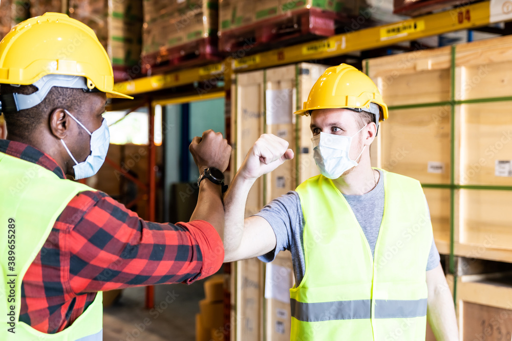 Interracial warehouse worker with face mask do elbow bump greeting Interracial warehouse worker with face mask do elbow bump greeting