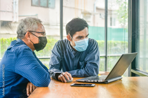 Asian man two people talking in office and working by computer notebook, Man face mask protect coronavirus covid 19