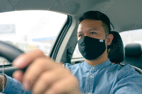 Asian man wears a black cloth mask. driving to pick up passengers. concept of coronavirus or COVID-19 protection on the taxi.