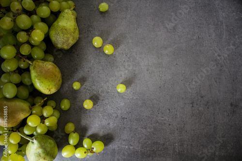 Still life with green pears and grapes on dark grey textured background. Summer fruits close up photo. 