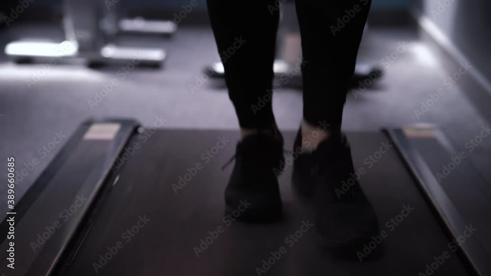 Female feet wearing black sneakers running on treadmill. Tilt down partial view of woman doing cardio exercises in gym. Concept of fitness Female feet wearing black sneakers running on treadmill. Tilt down partial view of woman doing cardio exercises in gym. Concept of fitness
