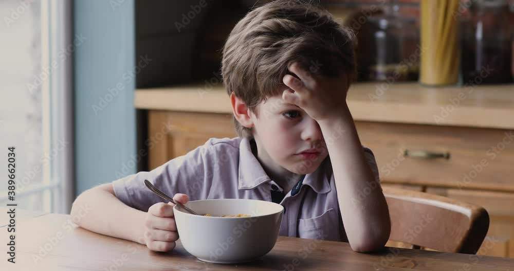 Little 7s boy sitting at dining table in kitchen in front of bowl with milk and cornflakes, kid feels sluggish without appetite lack of energy in the morning. Get up early, not tasty breakfast concept Little 7s boy sitting at dining table in kitchen in front of bowl with milk and cornflakes, kid feels sluggish without appetite lack of energy in the morning. Get up early, not tasty breakfast concept