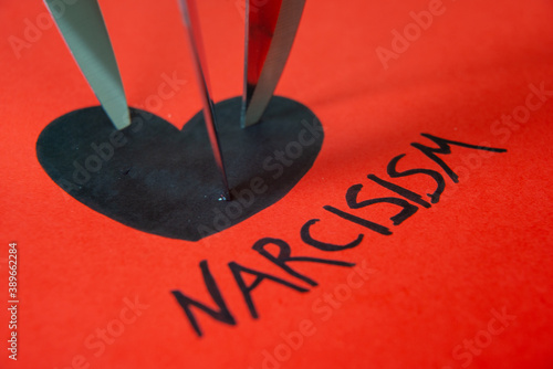 Word Narcisism, written in black on red paper, next to black heart drawing, with knife blades photo