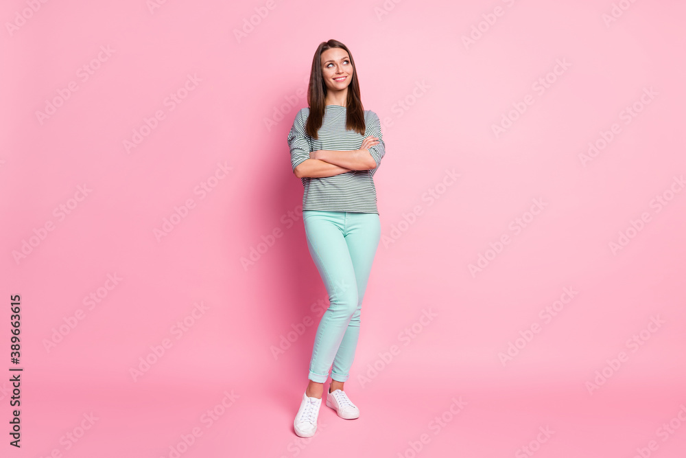 Full size photo of positive sweet girl stand crossed arms look empty space wear blue pants sneakers shirt isolated on pink color background
