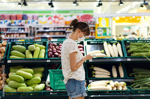 Obraz na płótnie Young woman with face mask using mobile phone and buying groceries in the supermarket w salonie