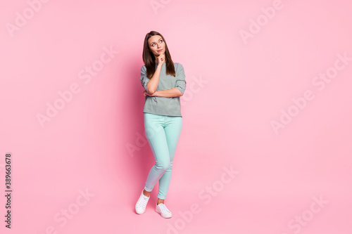 Full size photo of thinkable sweet girl stand look empty space wear blue pants sneakers shirt isolated on pink color background