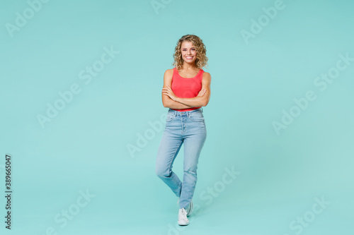 Full length of smiling charming beautiful attractive young blonde woman 20s wearing basic pink casual tank top jeans standing looking camera isolated on blue turquoise background, studio portrait.