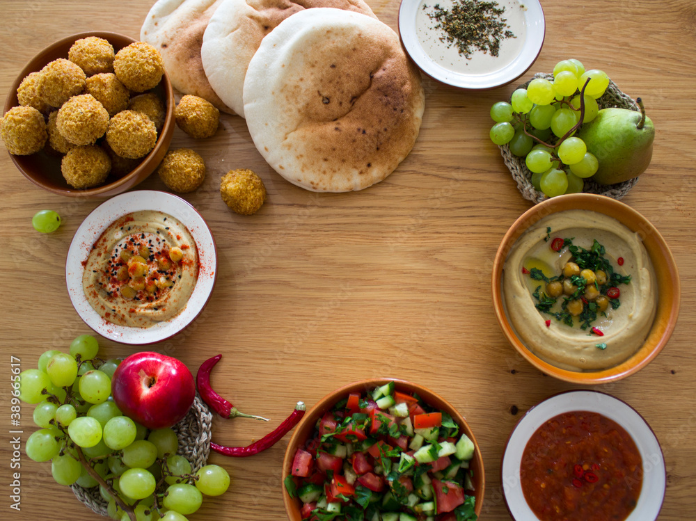 Food frame or border made of traditional Israeli meals: hummus, falafels, pita bread and different sauces on wooden table. Authentic dishes top view photo with copy space. 
