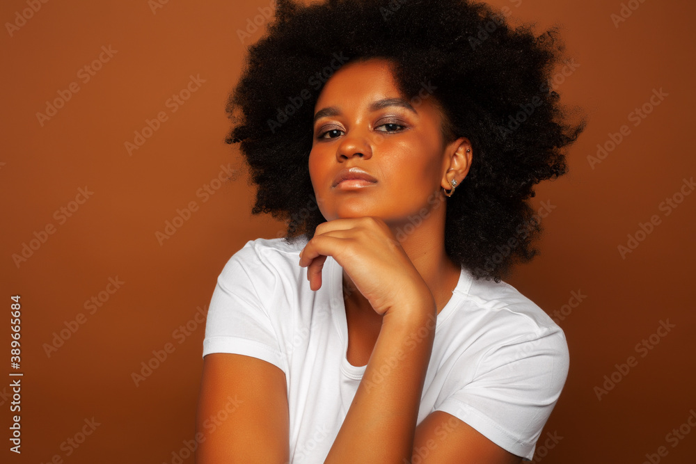 pretty young african american woman with curly hair posing cheerful gesturing on brown background, lifestyle people concept pretty young african american woman with curly hair posing cheerful gesturing on brown background, lifestyle people concept