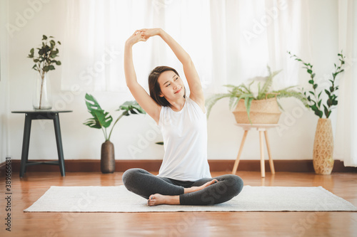 Smiling healthy Asian woman doing yoga shoulder stretching at home in living room