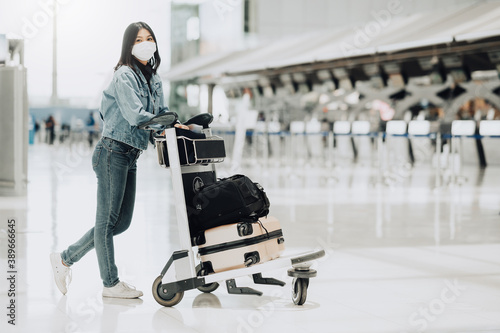 Happy Asian tourist woman with mask protection for coronavirus walking with luggage trolley ready for travel