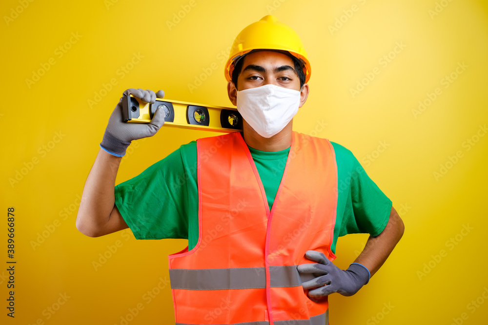 Asian constructor worker man with mask and safety vest hold waterpass on his shoulder Asian constructor worker man with mask and safety vest hold waterpass on his shoulder
