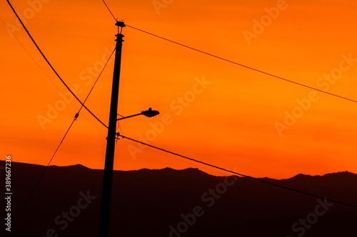 silhouettes of a sunset with a lamp post and cables, light of