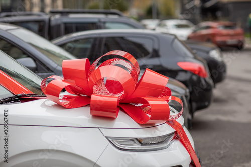 a white car with a big, red bow on the hood is on the street, an expensive gift, a new car as a gift, a gift car
