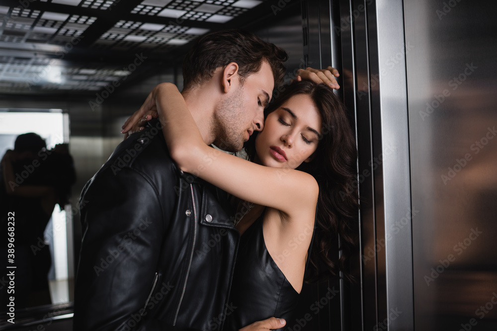 Passionate man in black jacket embracing sexy woman with closed eyes in elevator