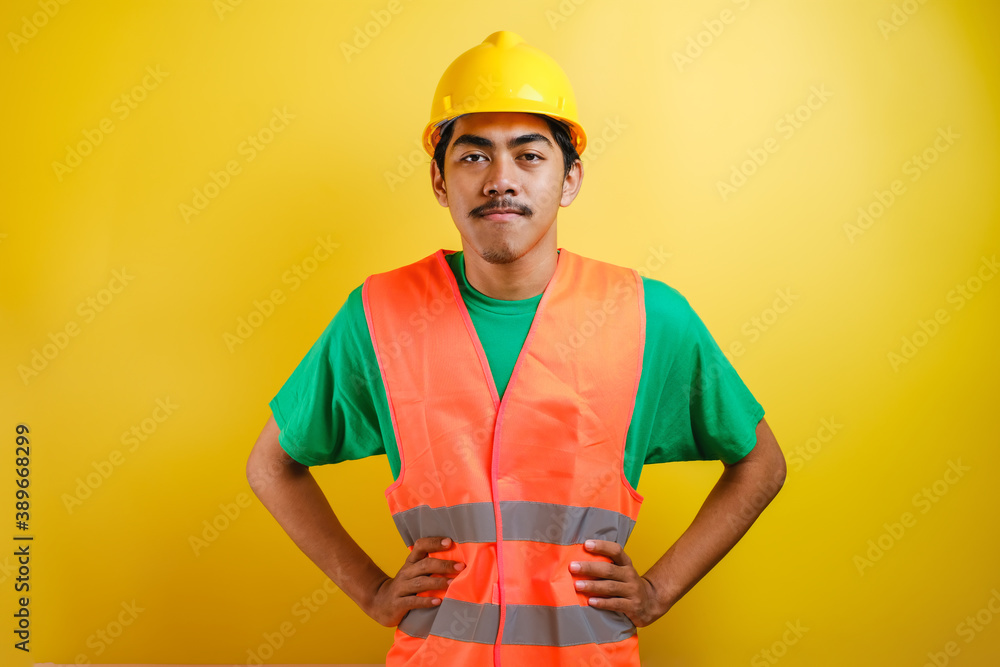 Asian construction worker smile looking to camera placing his both hand on his waist - obrazy, fototapety, plakaty 