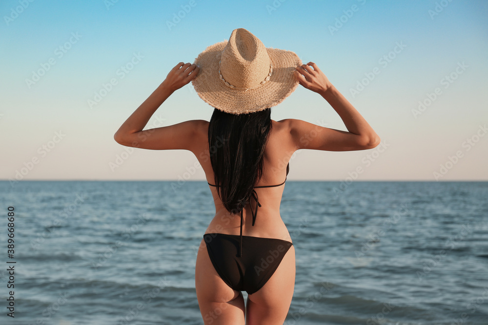 Young woman in black stylish bikini on beach, back view