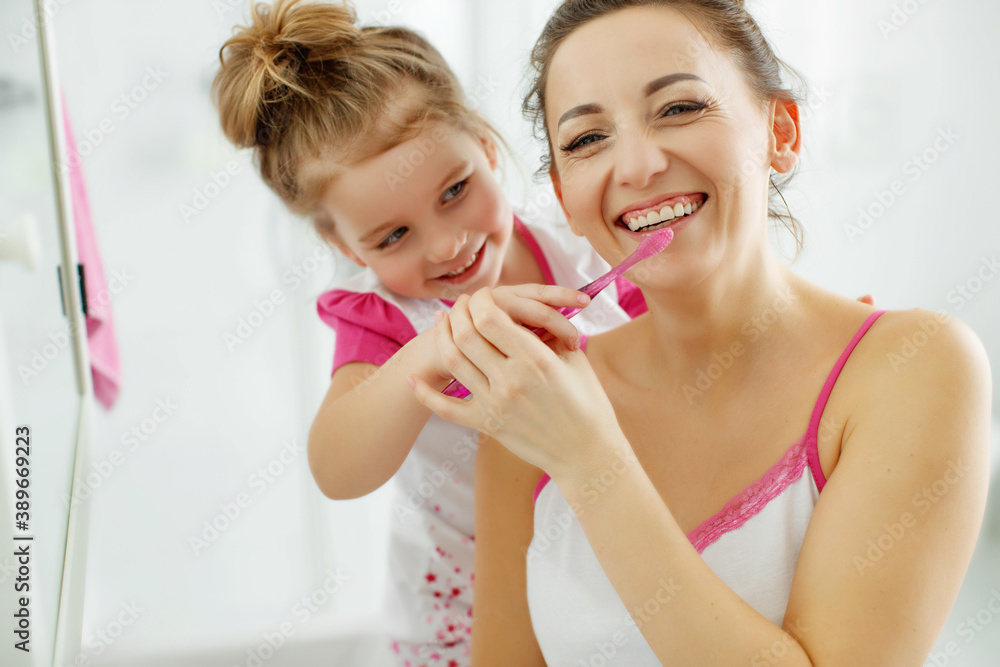Mother and her daughter brush their teeth with toothbrushes in the bathroom at home. Mom and baby girl in home clothes. High quality photo. Mother and her daughter brush their teeth with toothbrushes in the bathroom at home. Mom and baby girl in home clothes. High quality photo.