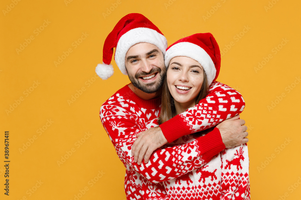 Smiling cheerful young Santa couple friends man woman 20s wearing red sweater Christmas hat hugging isolated on yellow background studio portrait. Happy New Year celebration merry holiday concept. Smiling cheerful young Santa couple friends man woman 20s wearing red sweater Christmas hat hugging isolated on yellow background studio portrait. Happy New Year celebration merry holiday concept.