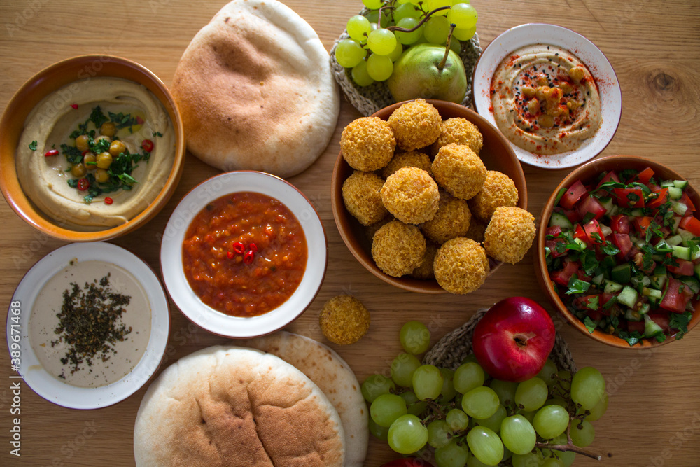   Authentic food of Middle East. Plate of hummus, falafels, pita bread, harissa sauce, tahini, fresh salad and fruits on wooden table. Traditional meals of Israel top view photo. Beautiful food pictur