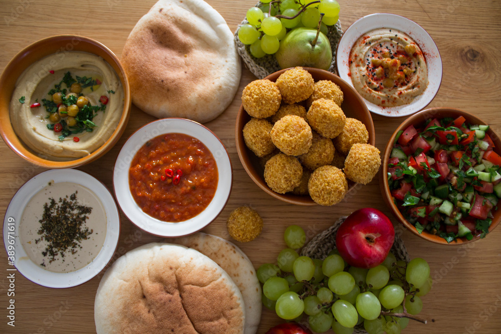 Authentic food of Middle East. Plate of hummus, falafels, pita bread, harissa sauce, tahini, fresh salad and fruits on wooden table. Traditional meals of Israel top view photo. Beautiful food pictur Authentic food of Middle East. Plate of hummus, falafels, pita bread, harissa sauce, tahini, fresh salad and fruits on wooden table. Traditional meals of Israel top view photo. Beautiful food pictur