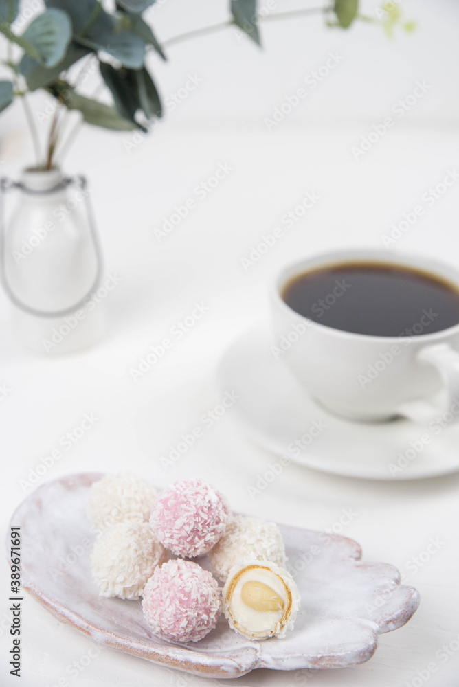 White coconut candy balls on handmade plate. Coconut cookies on white background with the cup of tea. Teapot with black tea. 
