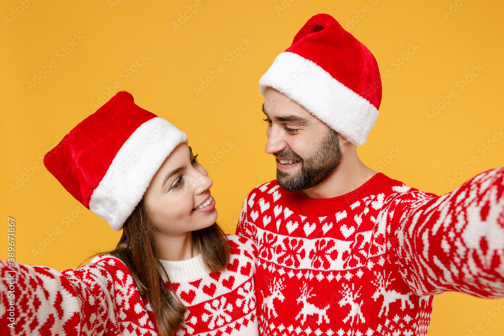 Close up smiling young Santa couple friends man woman in red sweater, Christmas hat doing selfie shot on mobile phone isolated on yellow background. Happy New Year celebration merry holiday concept. Close up smiling young Santa couple friends man woman in red sweater, Christmas hat doing selfie shot on mobile phone isolated on yellow background. Happy New Year celebration merry holiday concept.