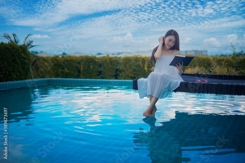 Portrait beautiful young Asian women reading a book on bed chair around the outdoor swimming pool.