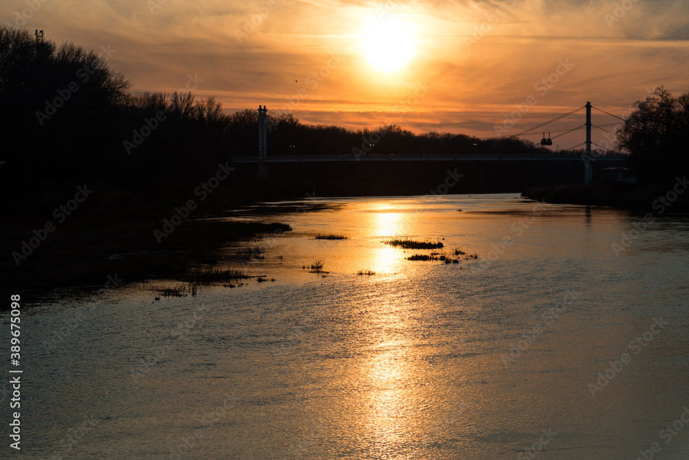 fiery sunset over the calmly flowing Ural river and pedestrian bridge