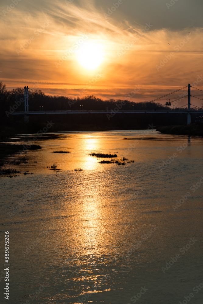 fiery sunset over the calmly flowing Ural river and pedestrian bridge