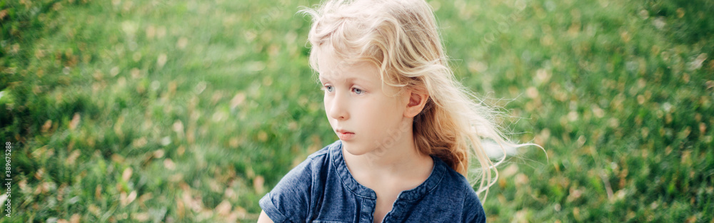 Portrait of blonde Caucasian thinking pensive child girl outdoor. Kid playing in park on a summer day. Authentic candid childhood moment. Web banner header. Portrait of blonde Caucasian thinking pensive child girl outdoor. Kid playing in park on a summer day. Authentic candid childhood moment. Web banner header.