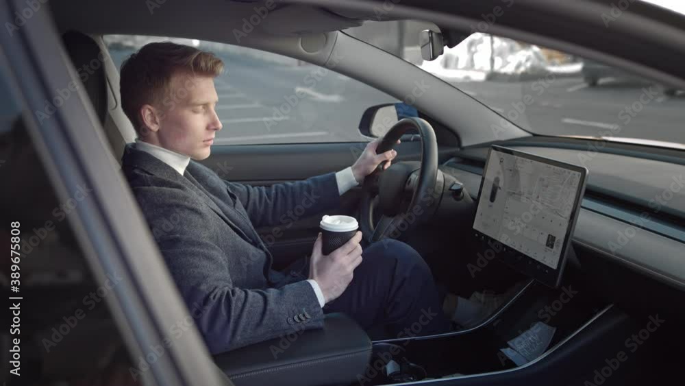 Portrait of a young successful man in the interior of a modern sports electric car. A man with coffee in his hands is focused, thinking about his future deal. Concept of: Business, Successful People Portrait of a young successful man in the interior of a modern sports electric car. A man with coffee in his hands is focused, thinking about his future deal. Concept of: Business, Successful People