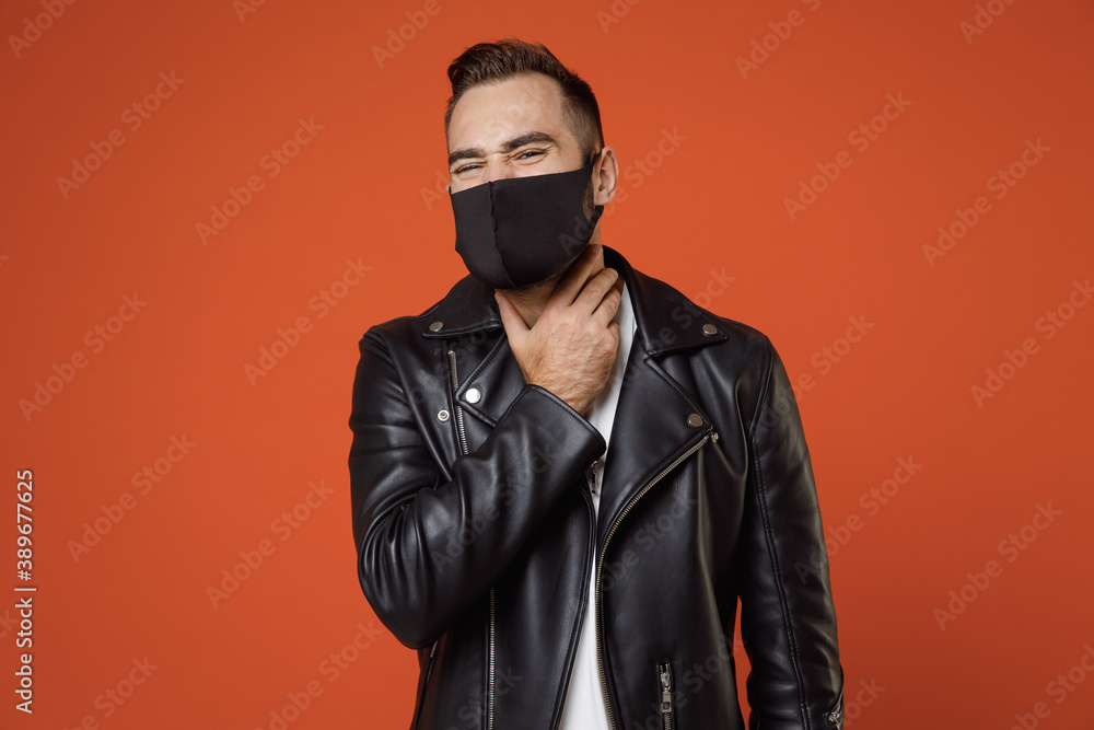 Sick young bearded man 20s in white t-shirt black leather jacket face mask safe from coronavirus virus covid-19 feeling sore throat, put hand on neck isolated on orange background studio portrait. Sick young bearded man 20s in white t-shirt black leather jacket face mask safe from coronavirus virus covid-19 feeling sore throat, put hand on neck isolated on orange background studio portrait.