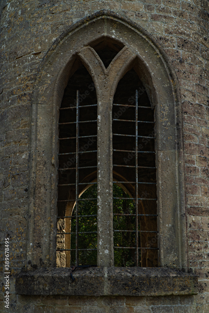 An old castle window seen from the outside of a turret with old arches and a narrow frame. Stone window with metal work.