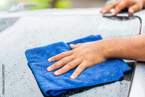 Hand holding blue cloth to cleaning wet body of modern car. Outdoor shooting in raining day.