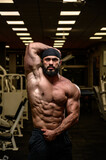 strong young athlete bearded male wearing bandana showing abdominal muscle in dark night gym